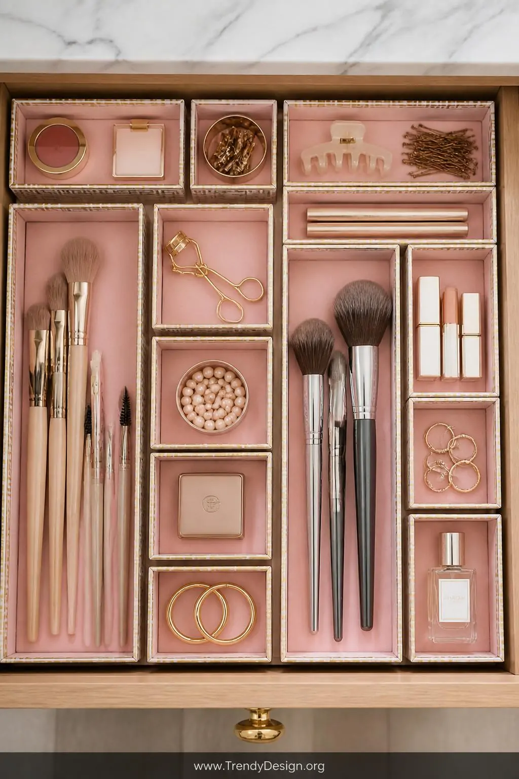 Slim cardboard organizer trays lined with blush pink contact paper arranged in a precise puzzle formation inside an open wooden drawer, washi tape borders in gold and white, overhead closeup shot revealing perfectly sorted makeup brushes and small accessories, photorealistic interior design