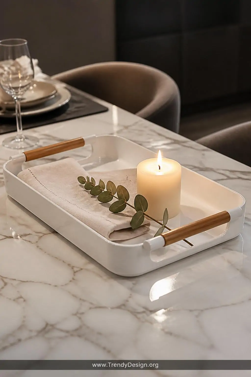 Glossy white spray-painted plastic bread tray serving tray with wooden handles on a marble dining table, styled with a folded cream linen napkin, a small lit pillar candle, and a sprig of eucalyptus, warm candlelight glow, closeup shot.
