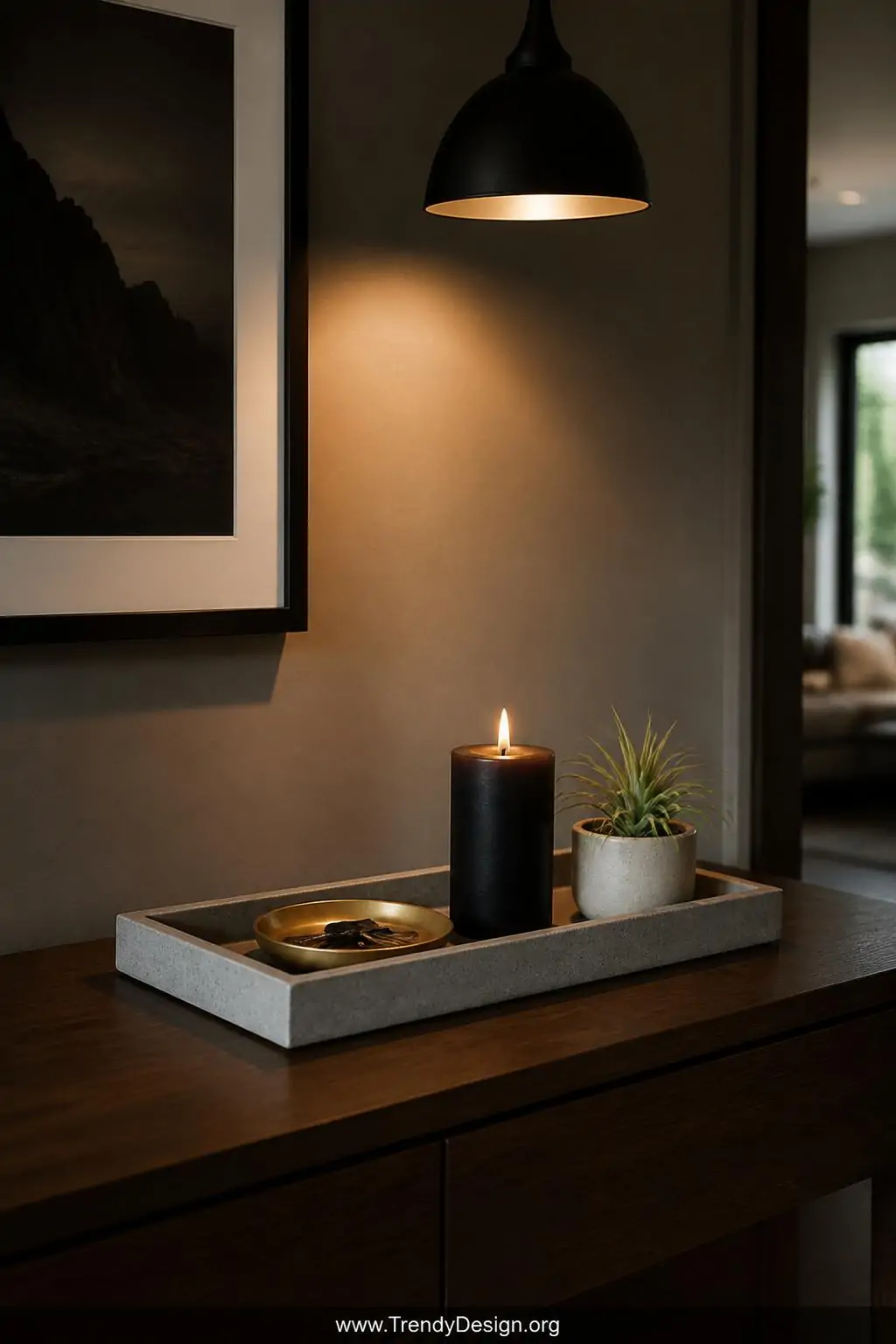 Sturdy rectangular concrete tray on a dark walnut entryway console table, holding a brushed brass key dish, a single lit black pillar candle, and a small air plant in a white ceramic pot, moody warm pendant light overhead, medium shot.
