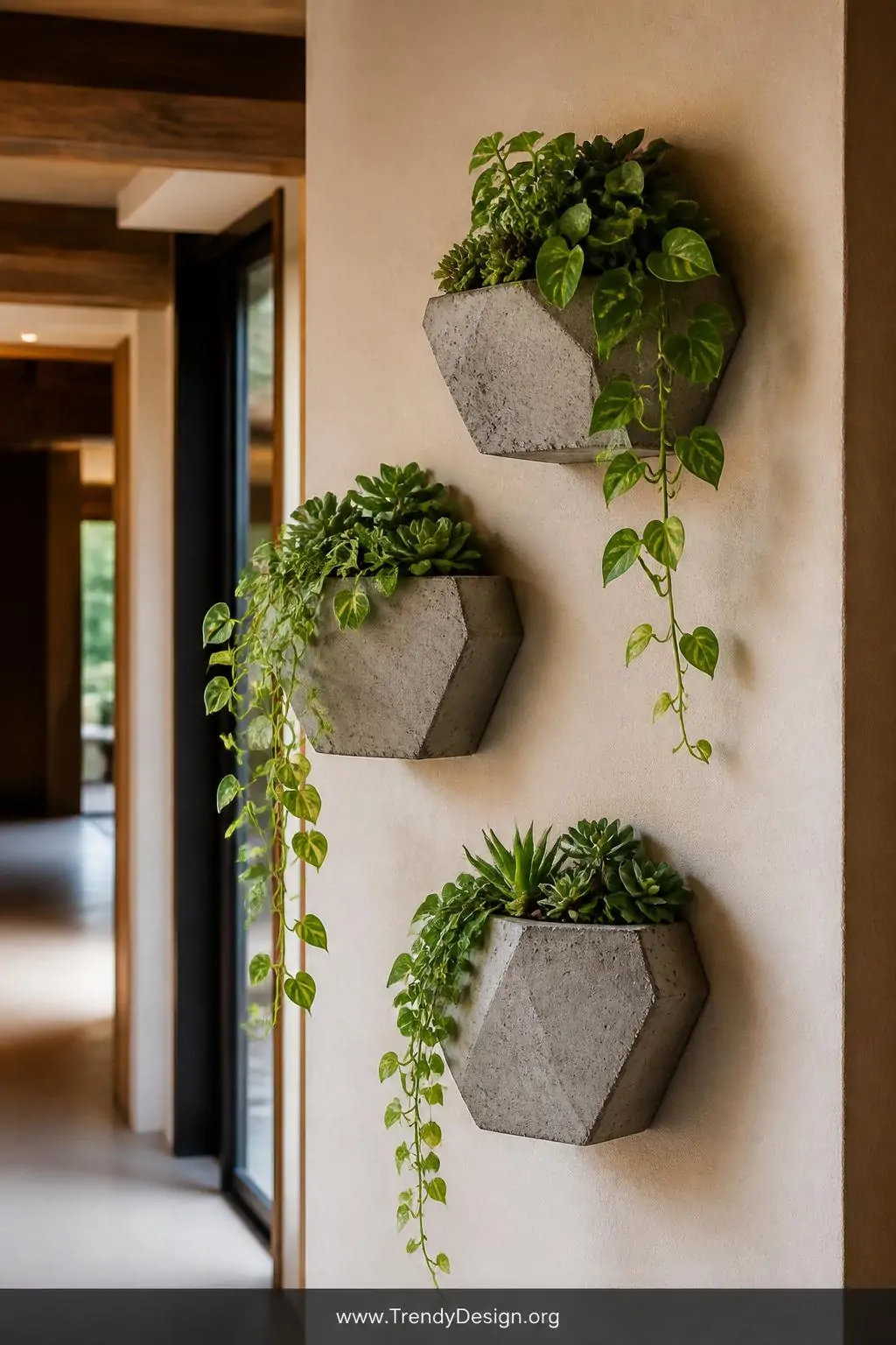 Three geometric concrete wall planters at staggered heights mounted on a warm-toned hallway wall, trailing pothos and small succulents spilling over rough gray hypertufa vessels, soft ambient natural light highlighting the contrast between textured concrete and lush green foliage, medium shot, photorealistic interior design, no people.