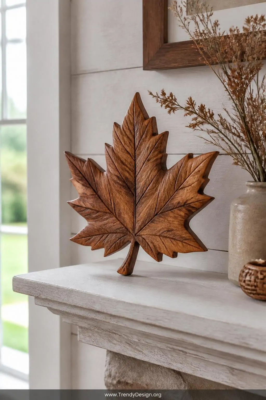Detailed relief-carved maple leaf with deep V-tool veining and thinned realistic edges displayed on a whitewashed mantelpiece beside dried botanicals, amber stain highlighting the grain, soft natural window light, medium shot