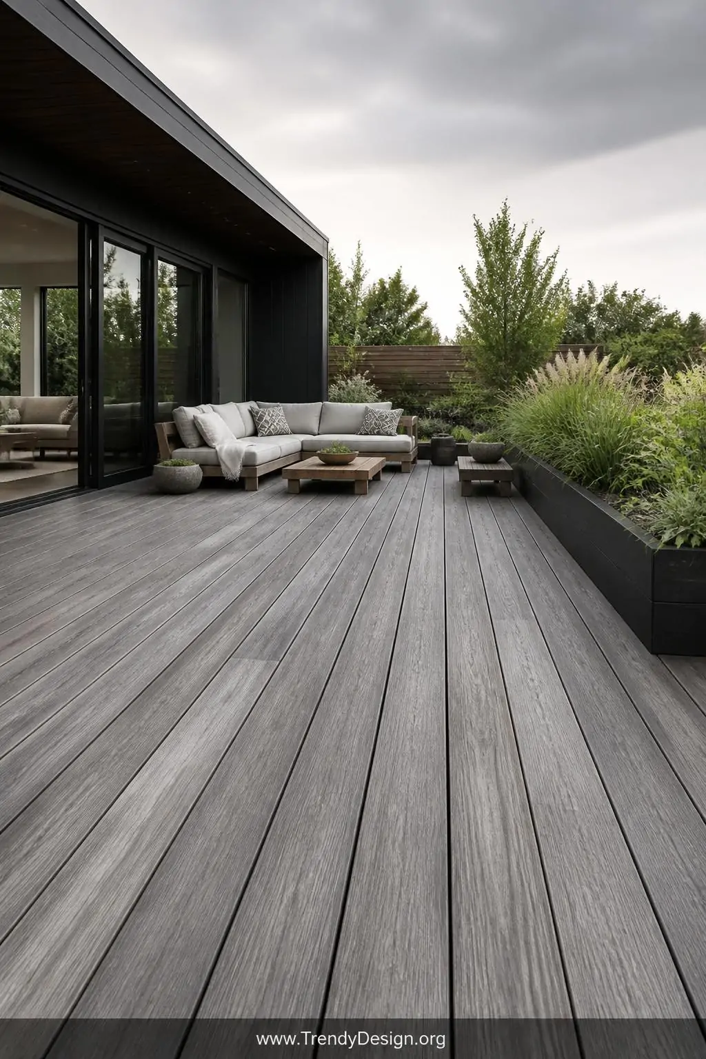 Gray weathered stained exterior deck boards on a modern outdoor deck, contemporary style, silvery driftwood-inspired semi-transparent finish soaked deep into the wood grain with no peeling edges, overcast natural daylight casting soft shadows across the polished low-maintenance surface, wide shot revealing the full deck expanse against clean architectural landscaping.