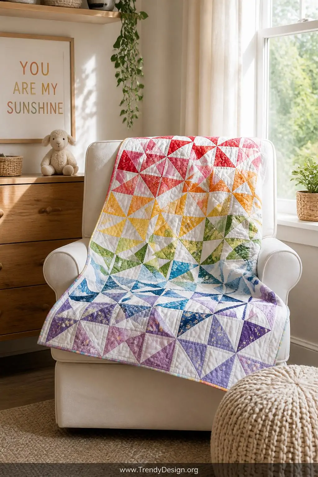 Pinwheel baby quilt laid across a white upholstered glider chair in a sunlit nursery corner, medium shot, rainbow gradient pinwheel blocks in crisp half-square triangles spinning against a consistent white background fabric, sharp pressed seam points catching warm afternoon light.