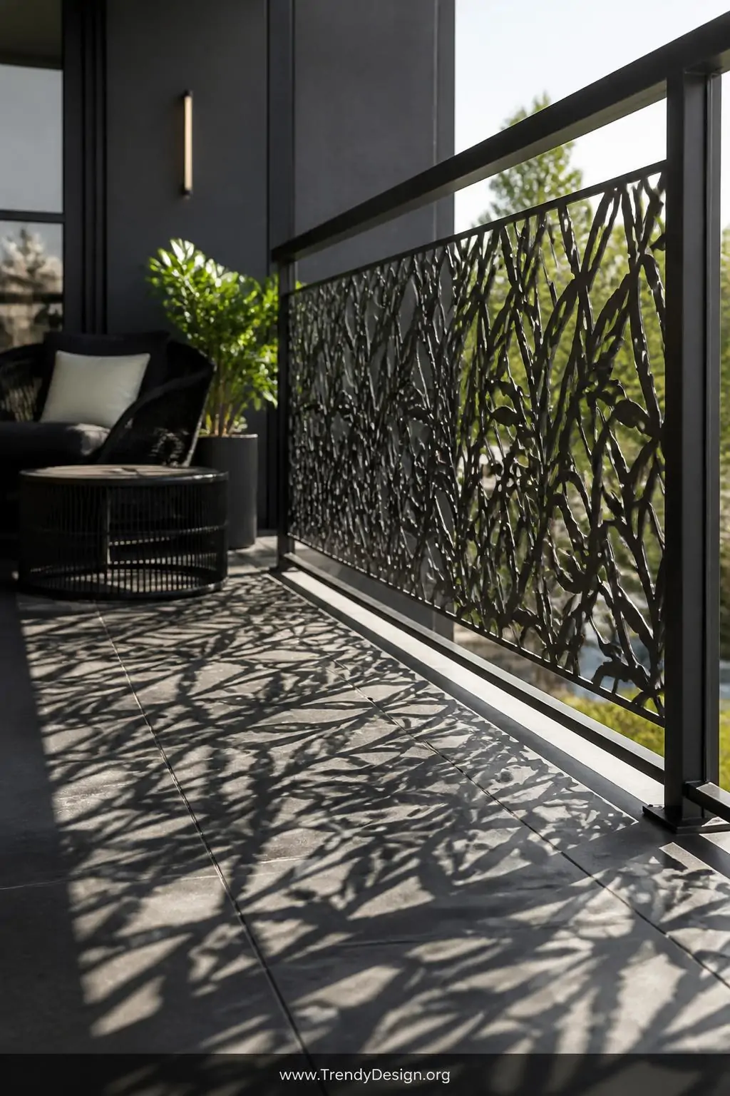 Laser-cut powder-coated steel privacy panel with an intricate botanical cutout pattern mounted to a balcony railing, architectural contemporary balcony, luxury modern style, complex geometric shadows cast across charcoal porcelain tile flooring, matte black metal furniture visible behind the panel, dramatic directional afternoon sun, medium shot.