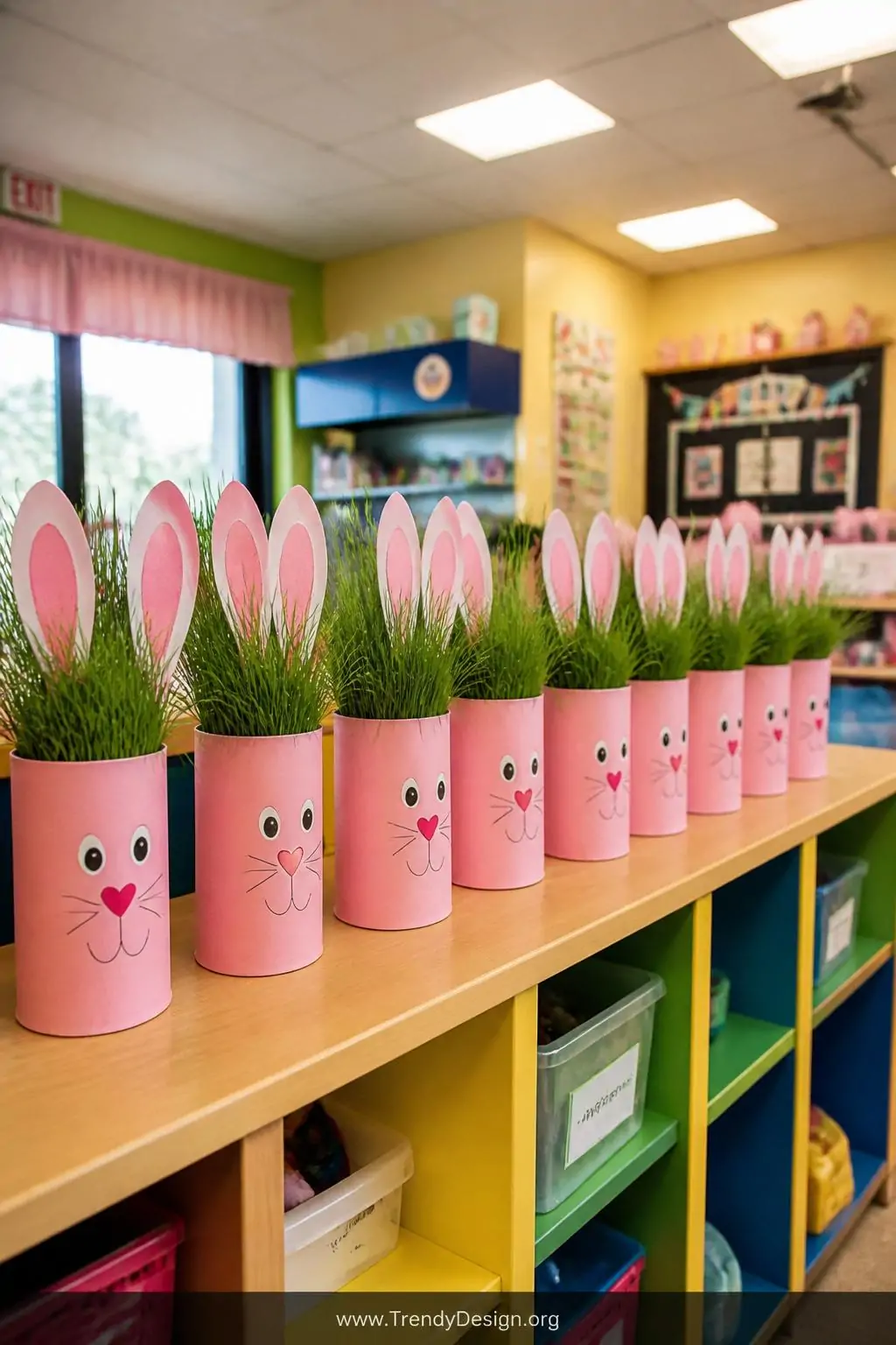 Toilet paper roll bunny grass head animals covered in pastel pink paper with folded ears and hand-drawn faces lined up along a colorful classroom shelf, warm overhead fluorescent lighting, dense green grass tufts crowning each cylindrical character, wide shot.