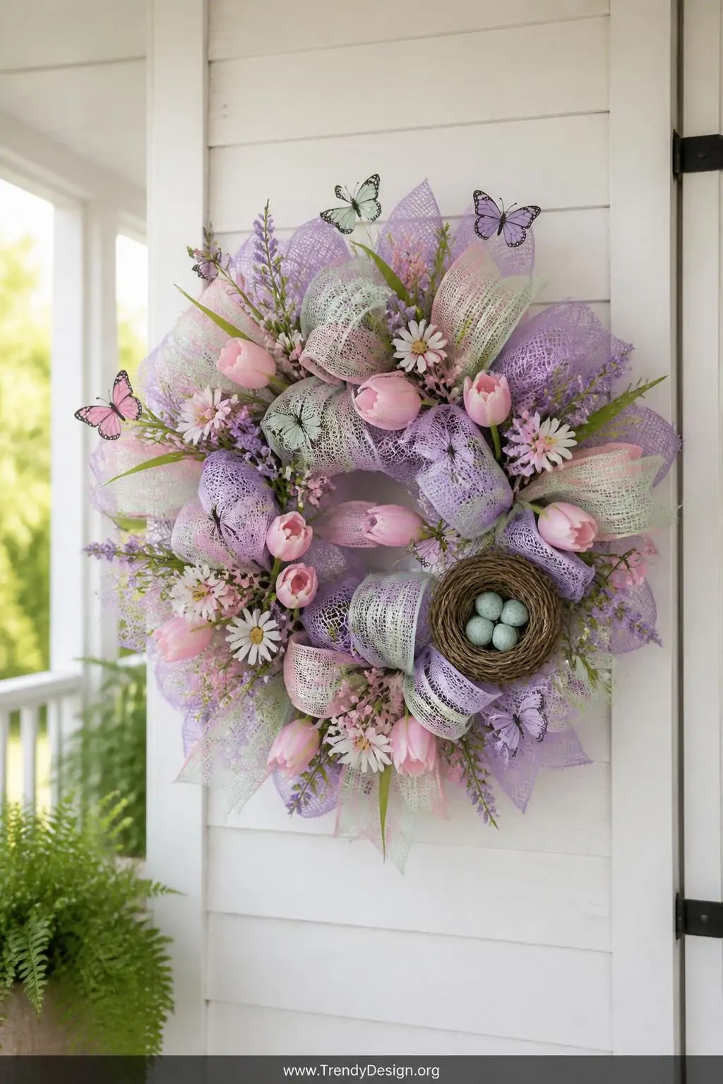 Soft lavender, pastel pink, and mint green deco mesh wreath with faux tulips, daisies, butterfly picks mid-flight, and a robin egg nest tucked to one side hanging on a white shiplap cottage door, soft natural morning light, medium shot.