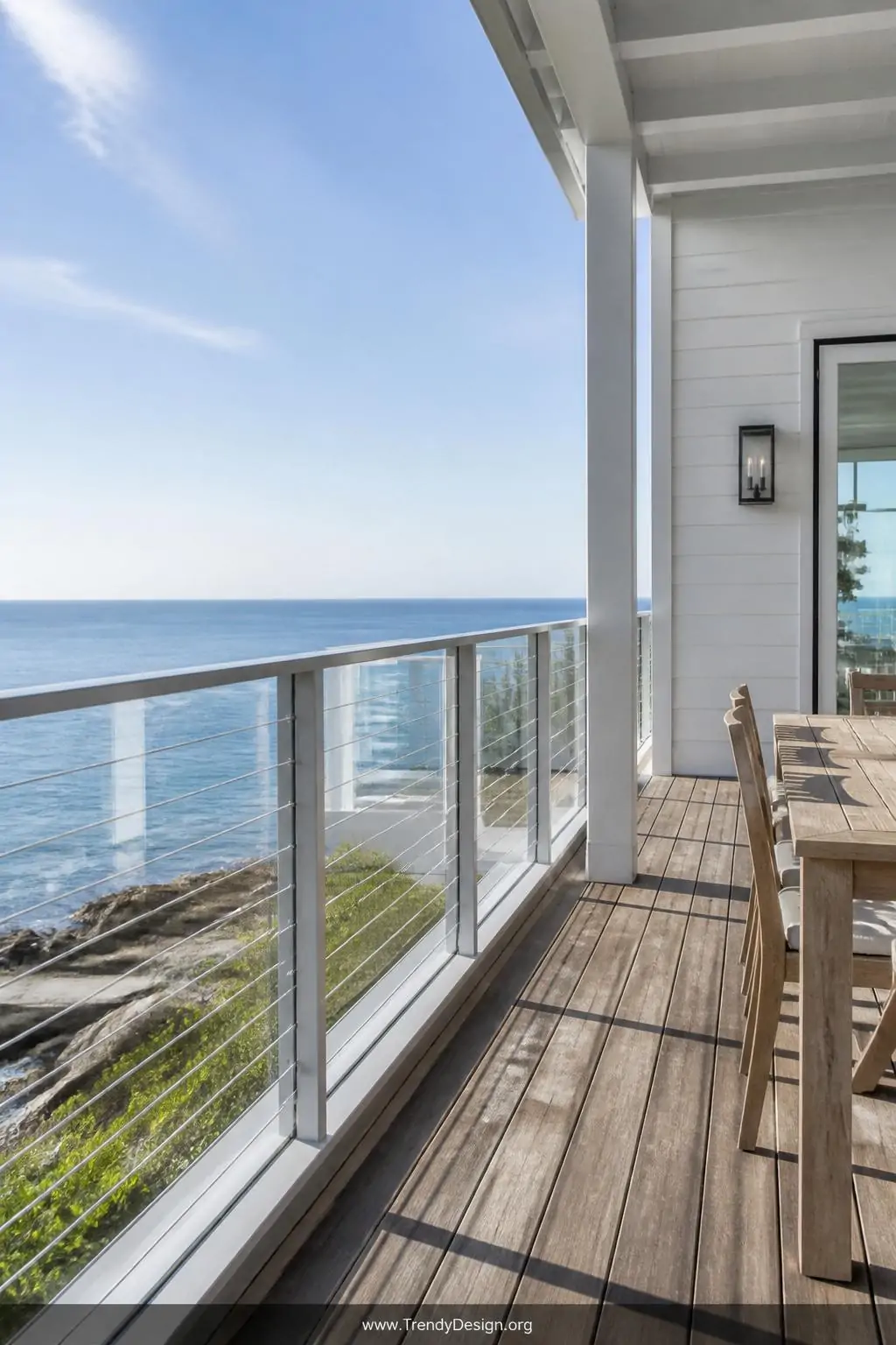 Wide photorealistic shot of a coastal contemporary deck featuring horizontal stainless steel cable lines layered across clear
