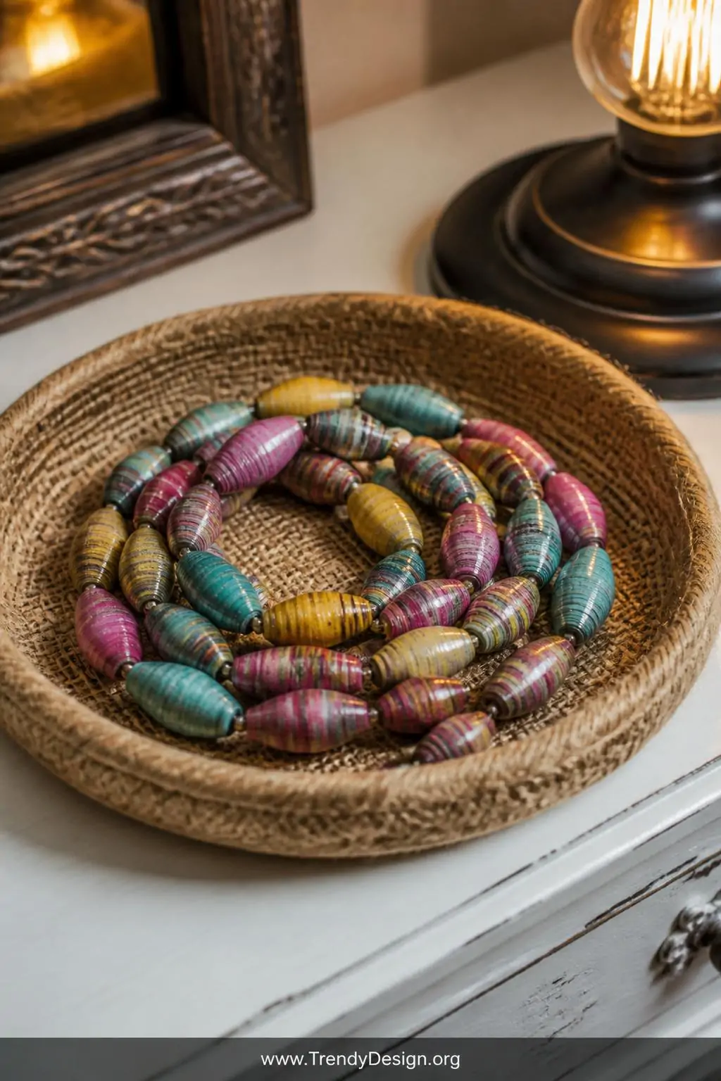 A close-up of a rustic jute-lined jewelry dish on a white painted dresser displays a coiled arrangement of handmade paper bea