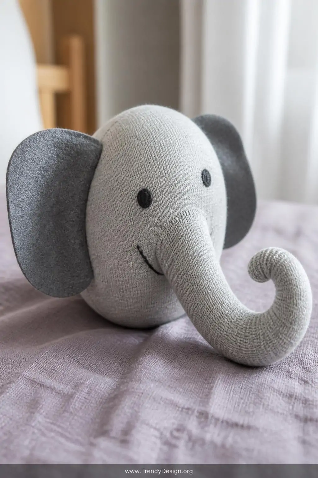 A photorealistic closeup shot of a sock elephant plushie resting on a dusty lavender linen surface, its gray cotton sock body