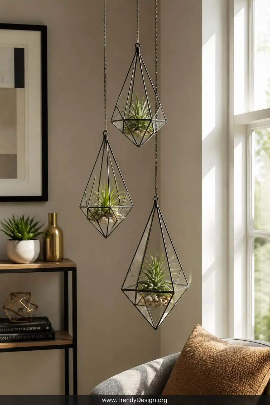 Three geometric diamond-shaped wire terrariums hanging at varying heights near a sunlit window, small succulents and air plants nestled inside delicate glass vessels cradled by the angular wire forms, modern minimalist living room with warm natural light, wide shot capturing the cascading cluster against a soft neutral wall.