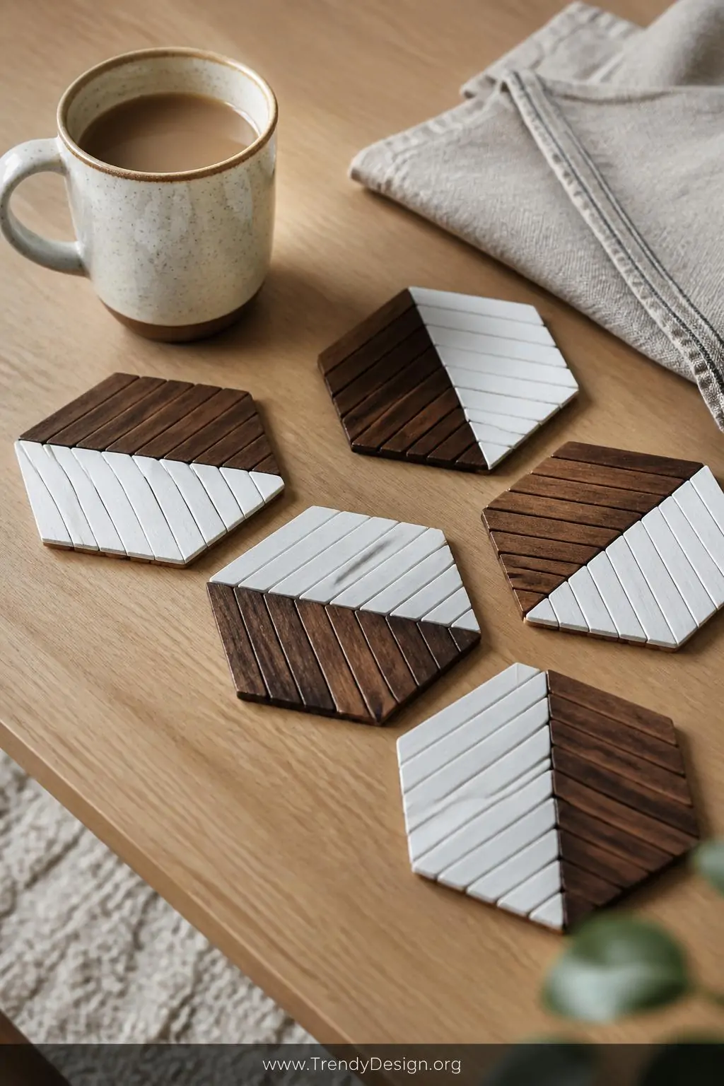 Set of six hexagonal popsicle stick coasters in an alternating herringbone pattern of dark walnut stain and crisp white paint arranged on a light oak coffee table beside a ceramic mug and a folded linen napkin, soft diffused natural light enhancing the two-tone wood texture and polished sealed surface, closeup shot.