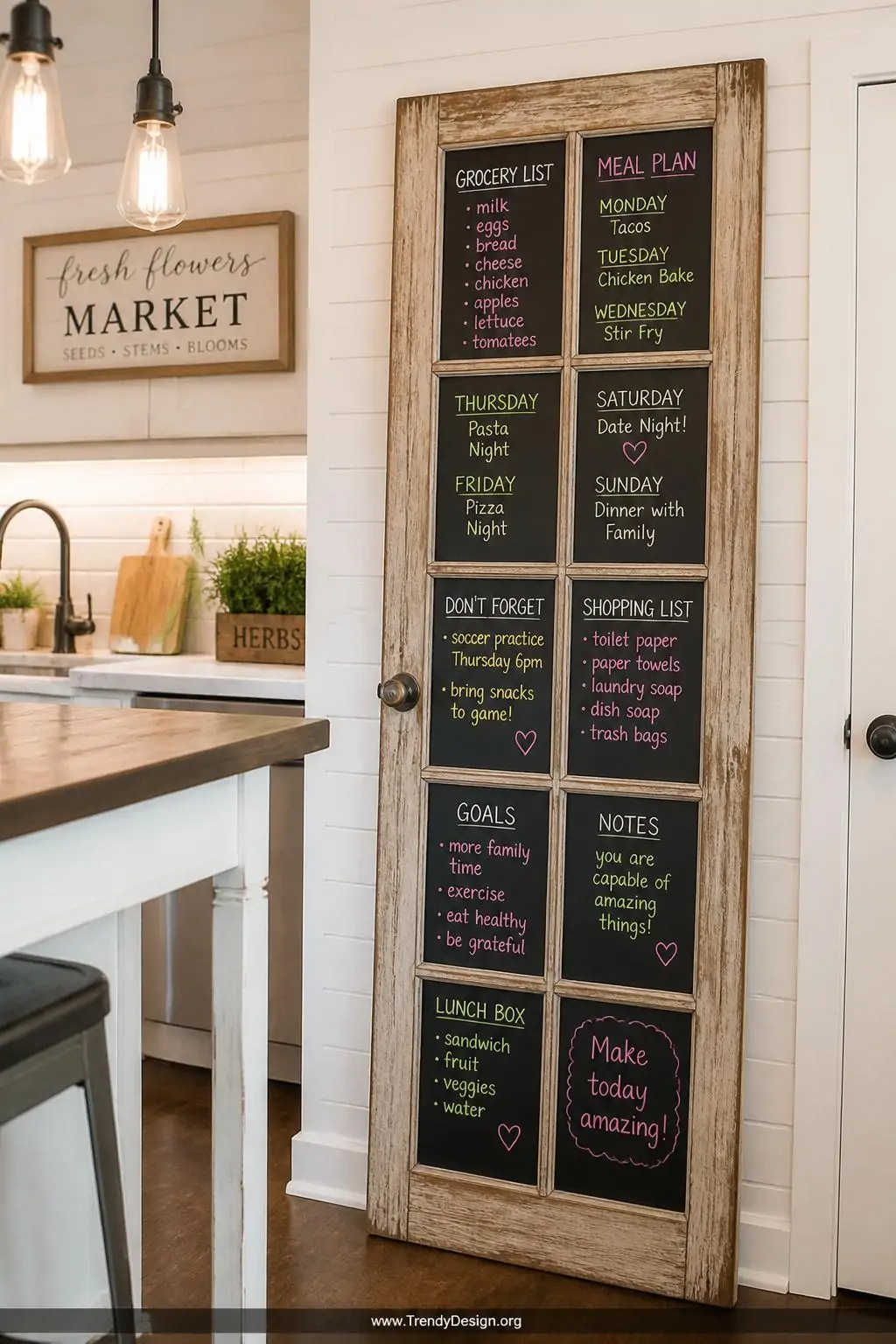 Repurposed French door with matte black chalkboard painted panes leaning against a bright farmhouse kitchen wall, colorful chalk marker writing filling each individual divided section with grocery lists and meal plans, warm overhead pendant lighting, medium shot, photorealistic interior design.