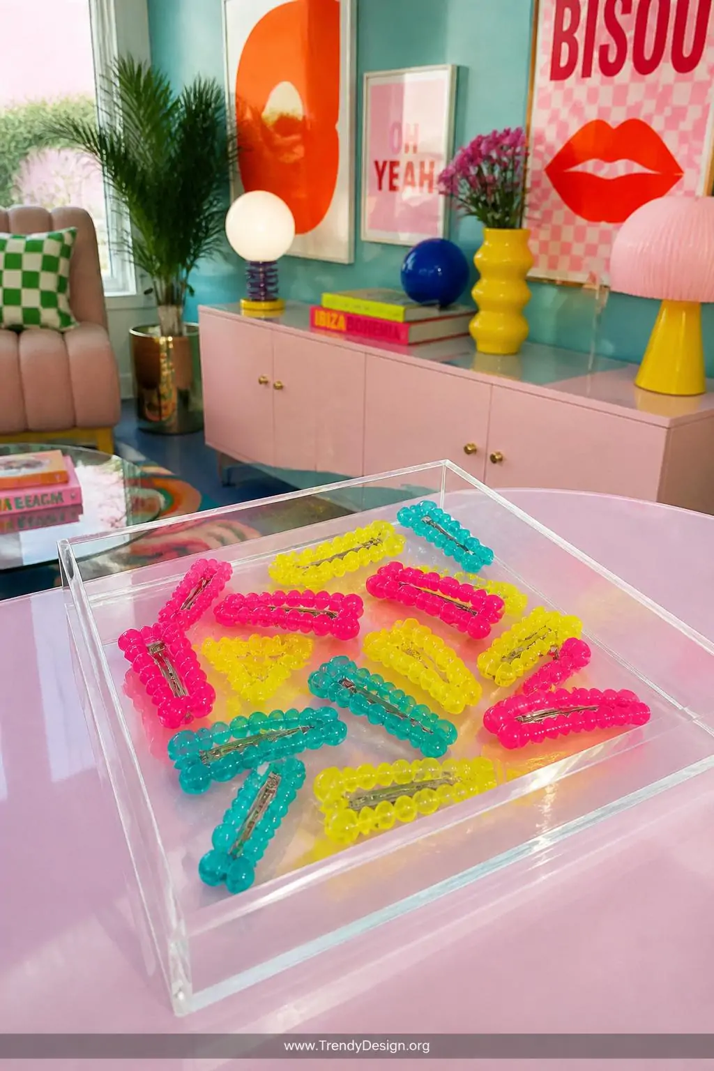 Cluster of chunky translucent hot pink, neon yellow, and turquoise plastic bead snap clips scattered across a glossy acrylic tray on a pastel laminate desk, bright overhead pop art inspired room with bold maximalist decor, wide shot.