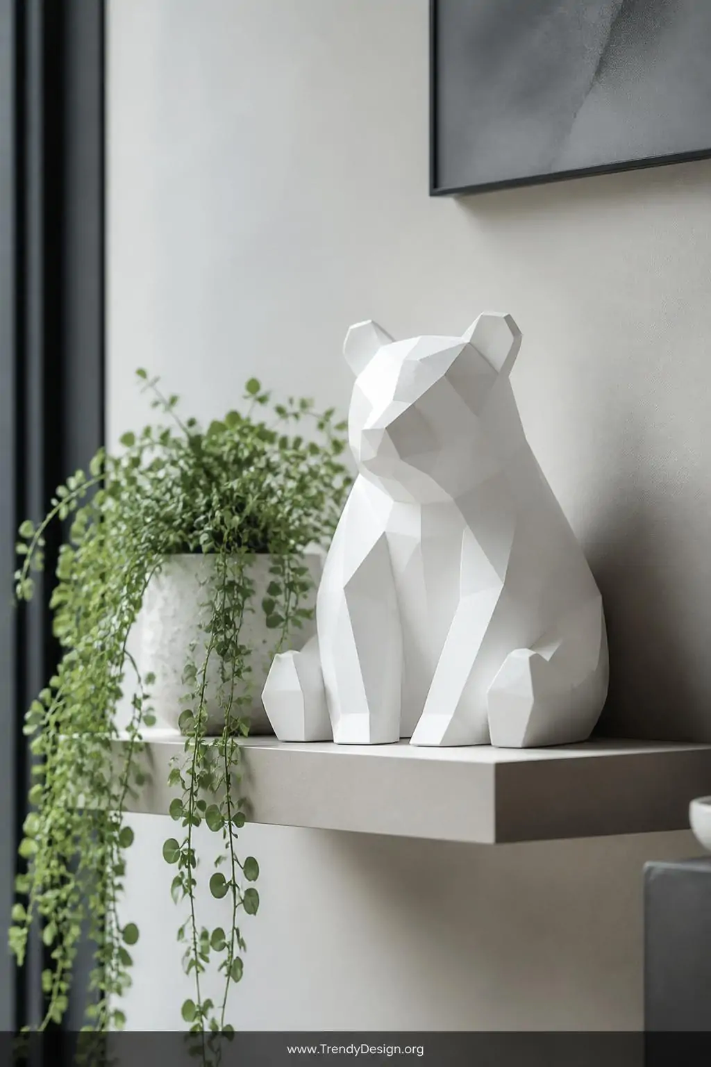 Matte white geometric clay bear figurine with angular flat planes and sharp sculptural edges displayed on a floating gallery shelf beside sage green trailing plants, clean cool studio lighting, medium shot