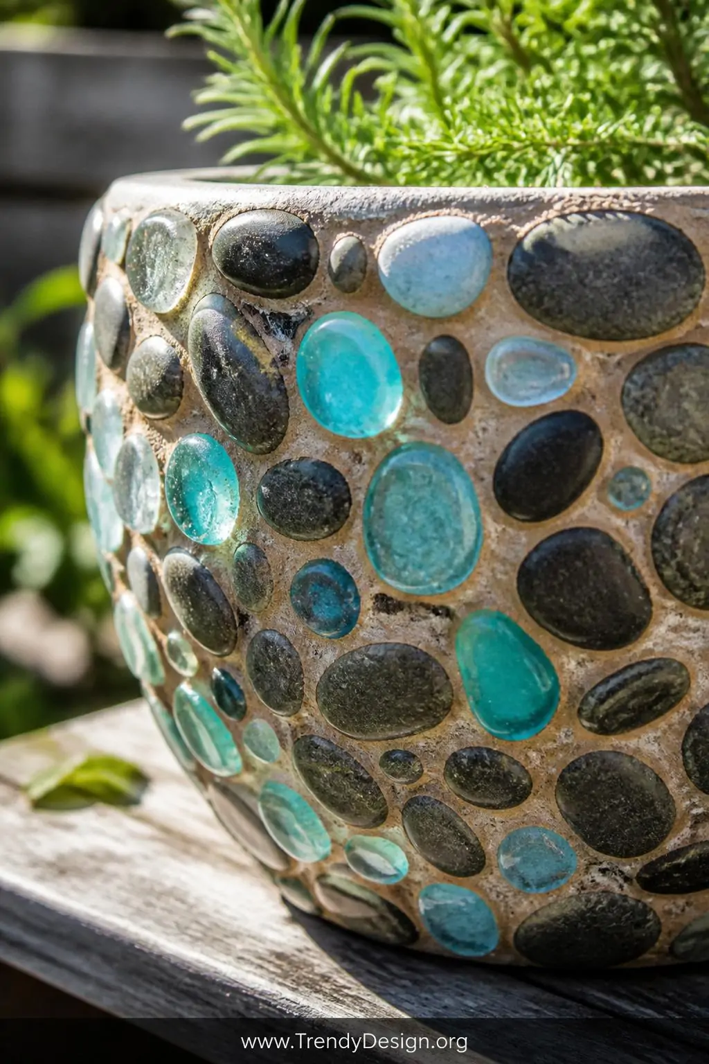A closeup detail shot of a handcrafted concrete pot encrusted with a mosaic of smooth multicolored river pebbles and turquois