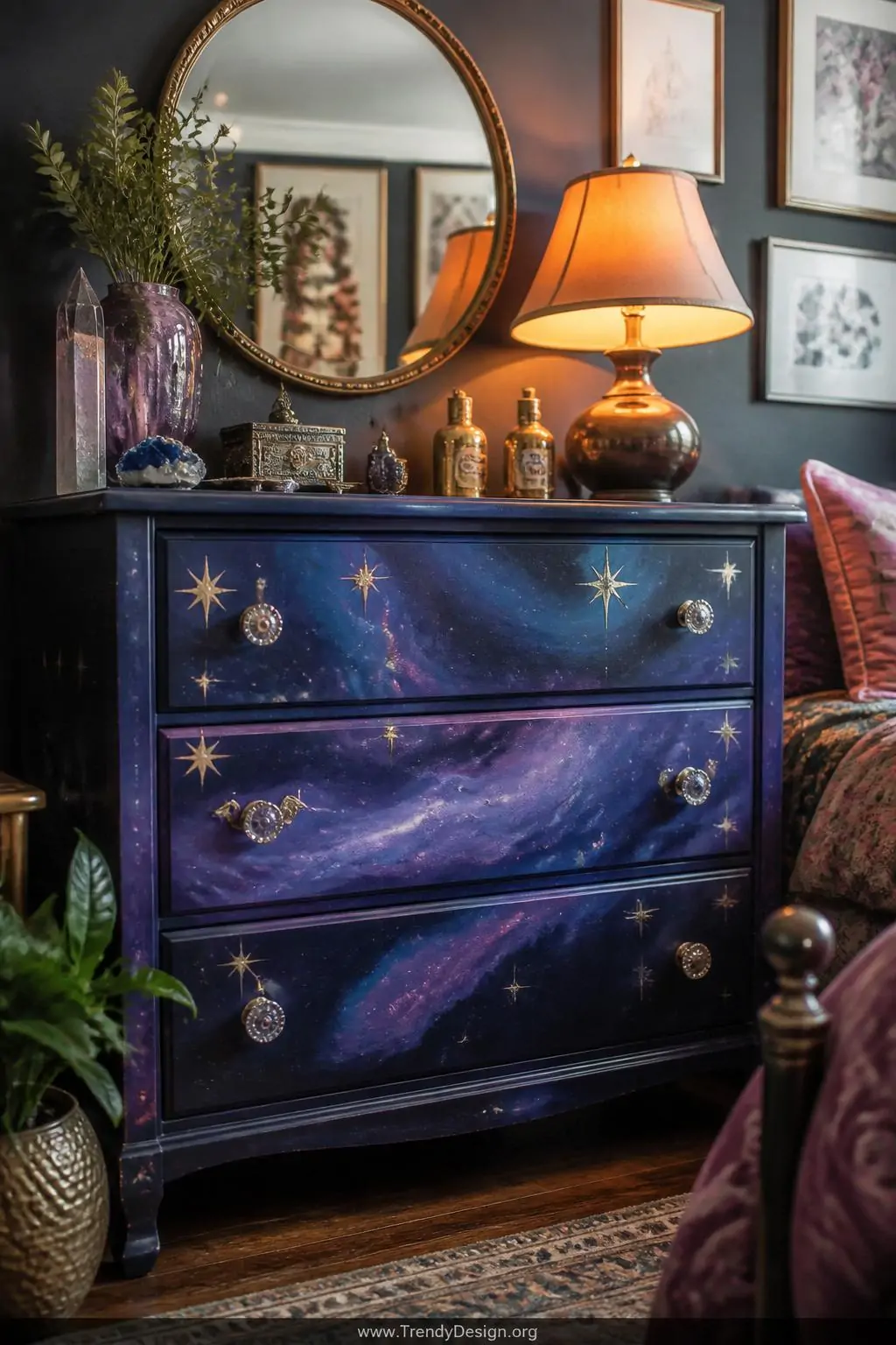 Thrift store wooden dresser painted with cosmic navy and purple swirling galaxy treatment, gold and silver metallic star accents catching a bedside lamp's warm glow in a maximalist bedroom corner, medium shot.