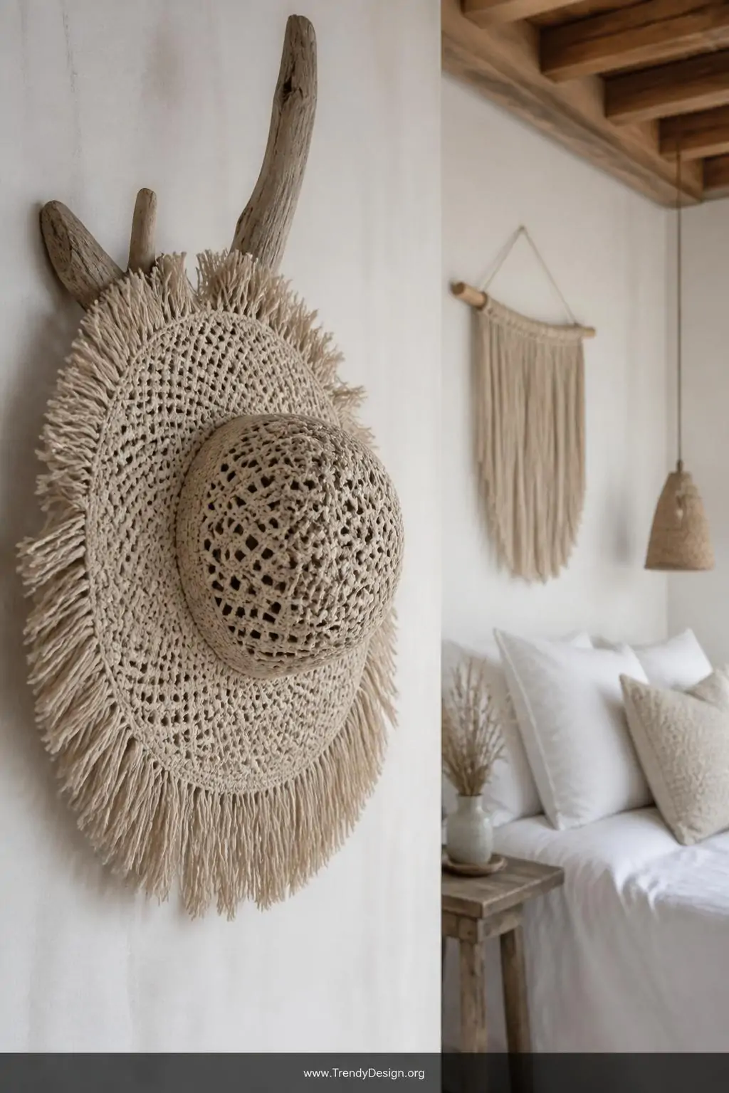 Natural cotton macramé sun hat with fringed brim hanging from a weathered driftwood hook against a whitewashed boho bedroom wall, soft diffused afternoon light, wide shot showcasing the earthy knotted texture and flowing fringe detail.