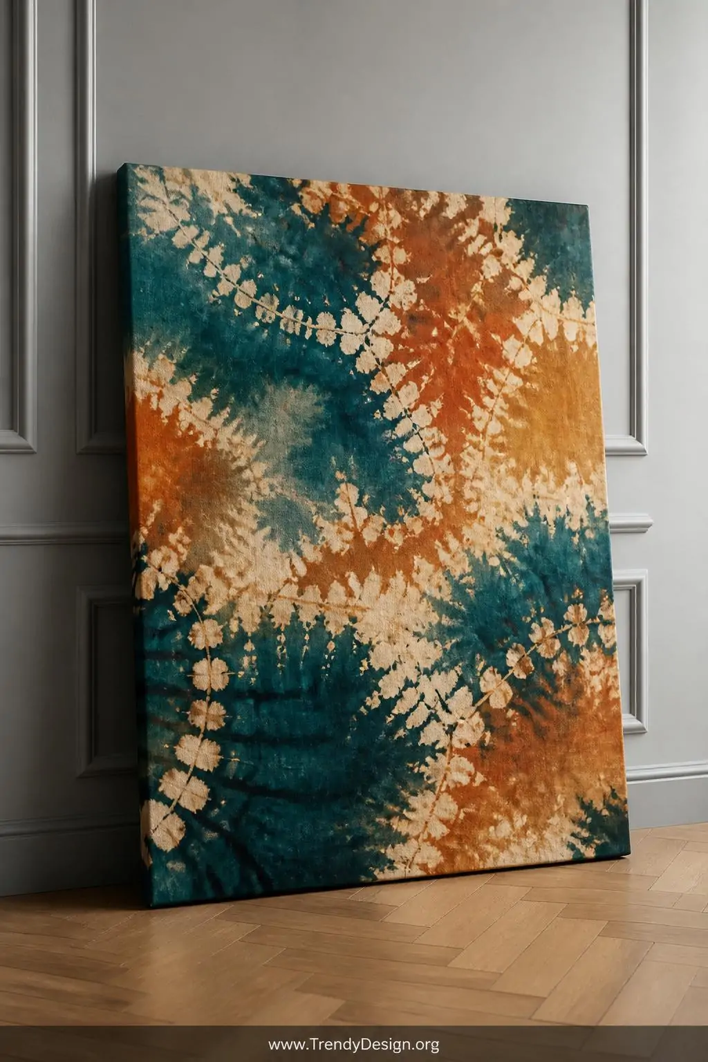 Stretched canvas print with wax resist watercolor pattern in deep teal, burnt sienna, and warm ivory revealing organic batik-style texture, leaning against a light grey gallery wall on a parquet floor, soft diffused studio lighting, wide shot