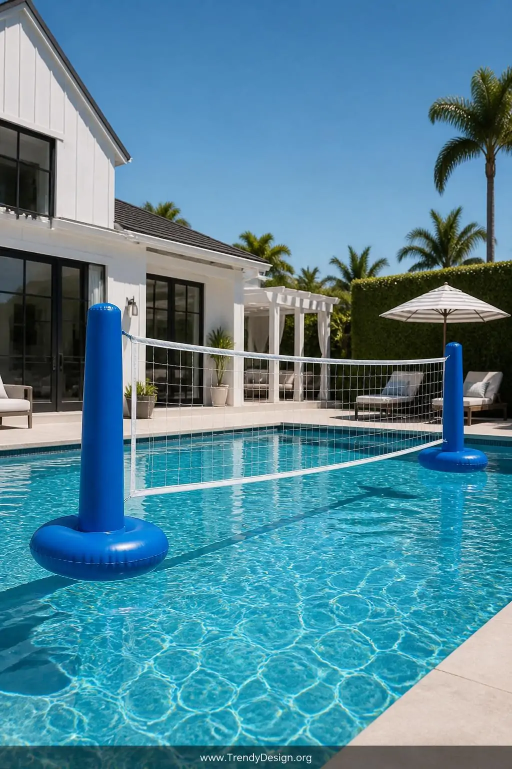 Inflatable pool volleyball net stretched across the middle of a sunlit backyard pool, outdoor recreational pool setting, energetic summer style, white mesh net strung between two bright blue inflatable poles with weighted bases resting on the pool floor, crisp blue water reflecting brilliant afternoon sky, wide shot