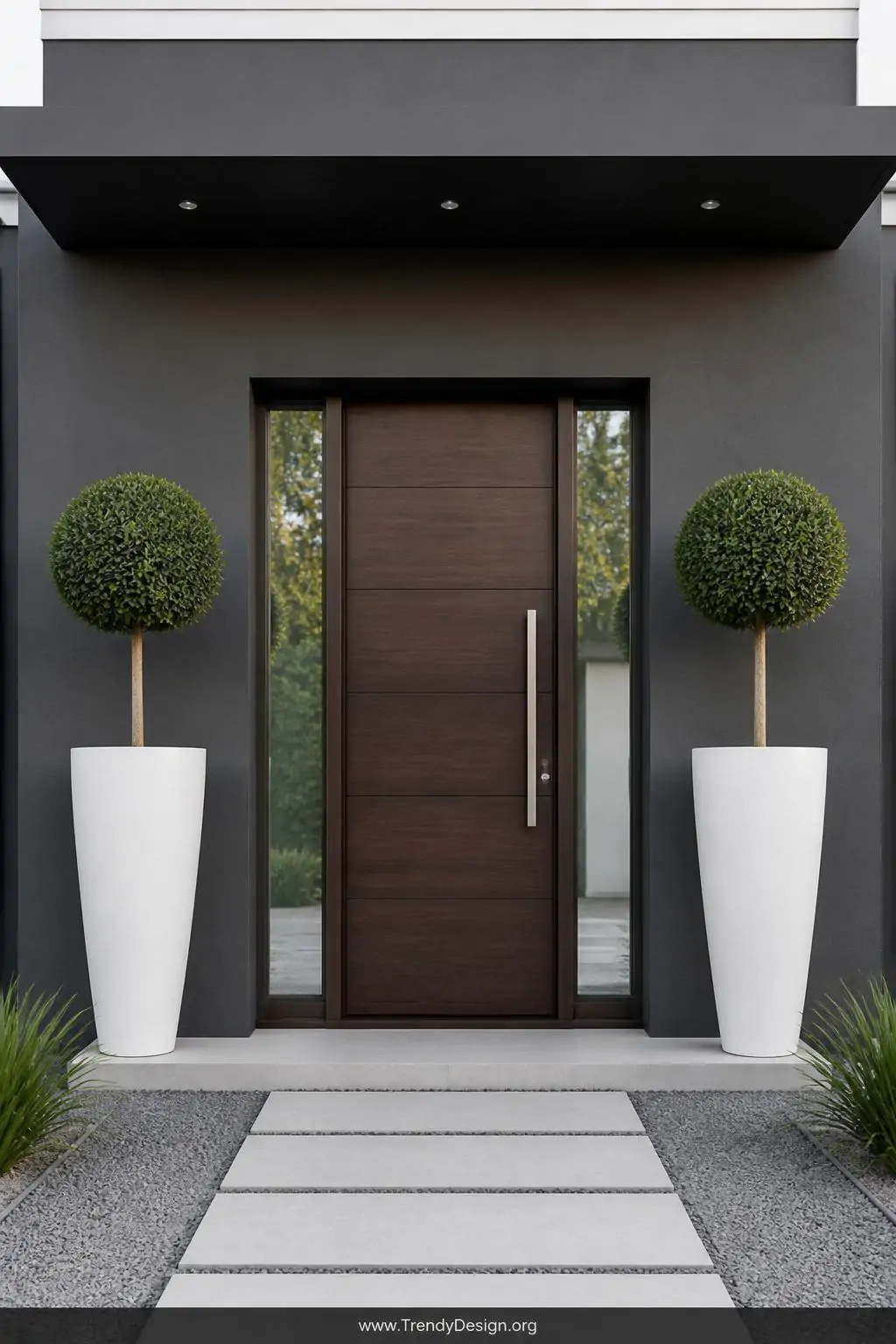 Pair of tall sleek white fiberglass column planters flanking a contemporary front door, wide shot, each holding a single sculptural lollipop topiary with a perfectly clipped dark green globe, clean architectural lines against a smooth charcoal gray facade, crisp even morning light emphasizing minimalist symmetry, photorealistic modern elegant entryway design.