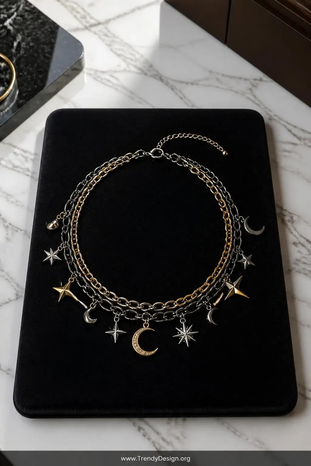 Mixed metal chain choker with gold and silver star and moon charms spread across a dark velvet jewelry board on a marble countertop, overhead soft white light, wide shot showcasing the edgy layered aesthetic and multiple pendant spacing