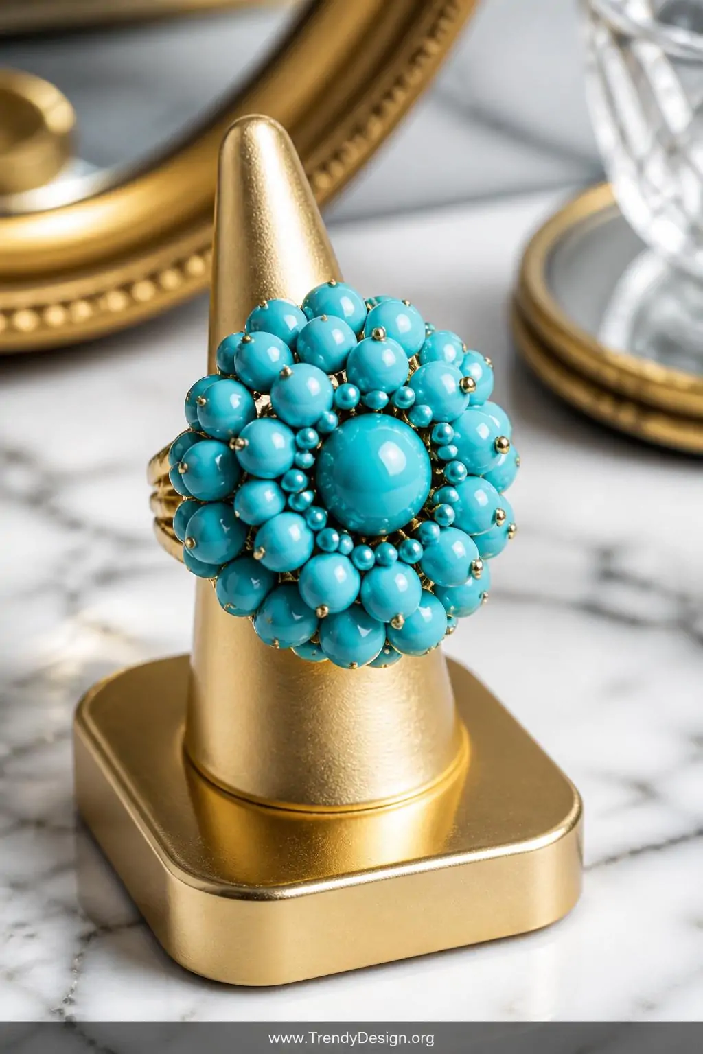 Bold turquoise bead cluster statement ring on a gold-toned ring display stand atop a marble vanity surface, bright overhead jewelry photography light, extreme closeup revealing the domed layered bead arrangement mixing matte and glossy turquoise finishes against the luxurious gold base.
