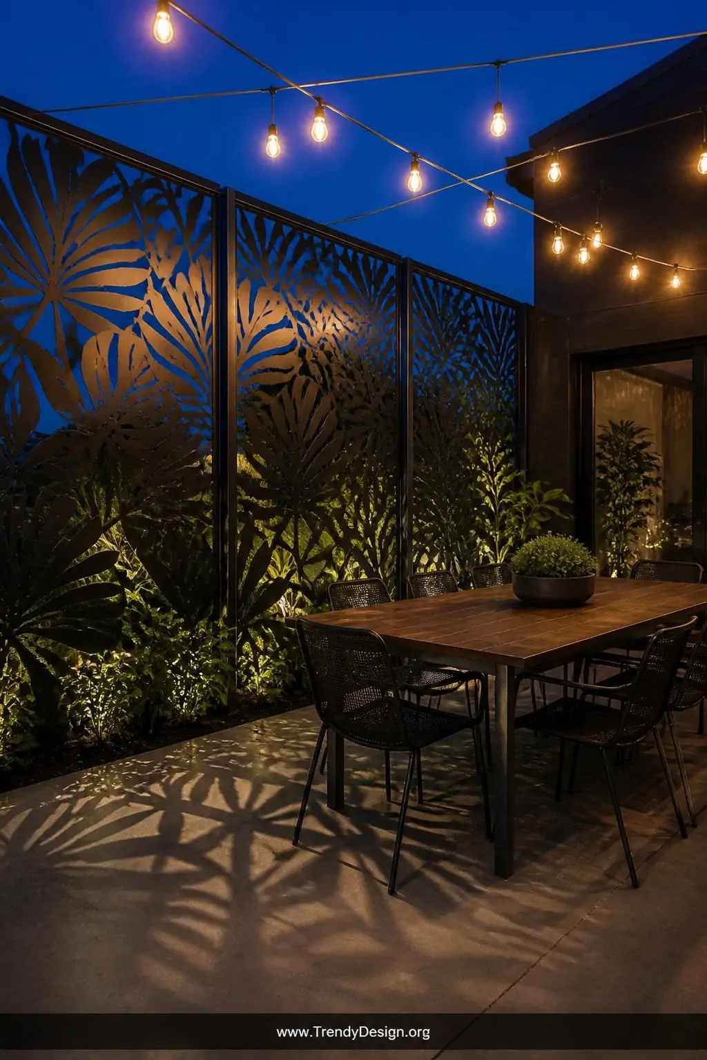 A dramatic medium-wide shot of a contemporary patio enclosed by matte black powder-coated laser-cut steel panels featuring an