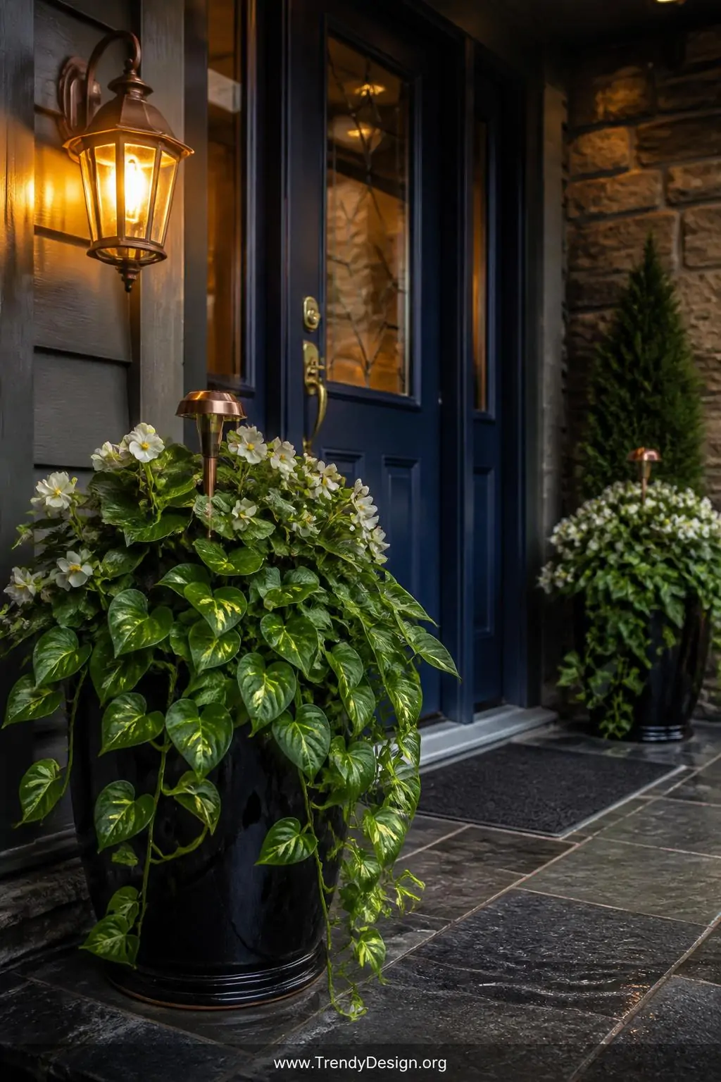A styled entryway wide shot featuring a glossy black metal planter bursting with trailing pothos and white-blooming begonias 