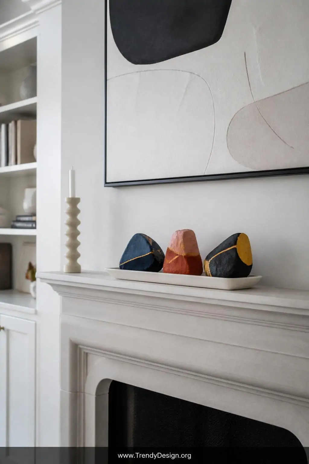 A wide shot of a minimalist living room mantelpiece lined with abstract color-blocked rocks in navy and gold, blush and terra