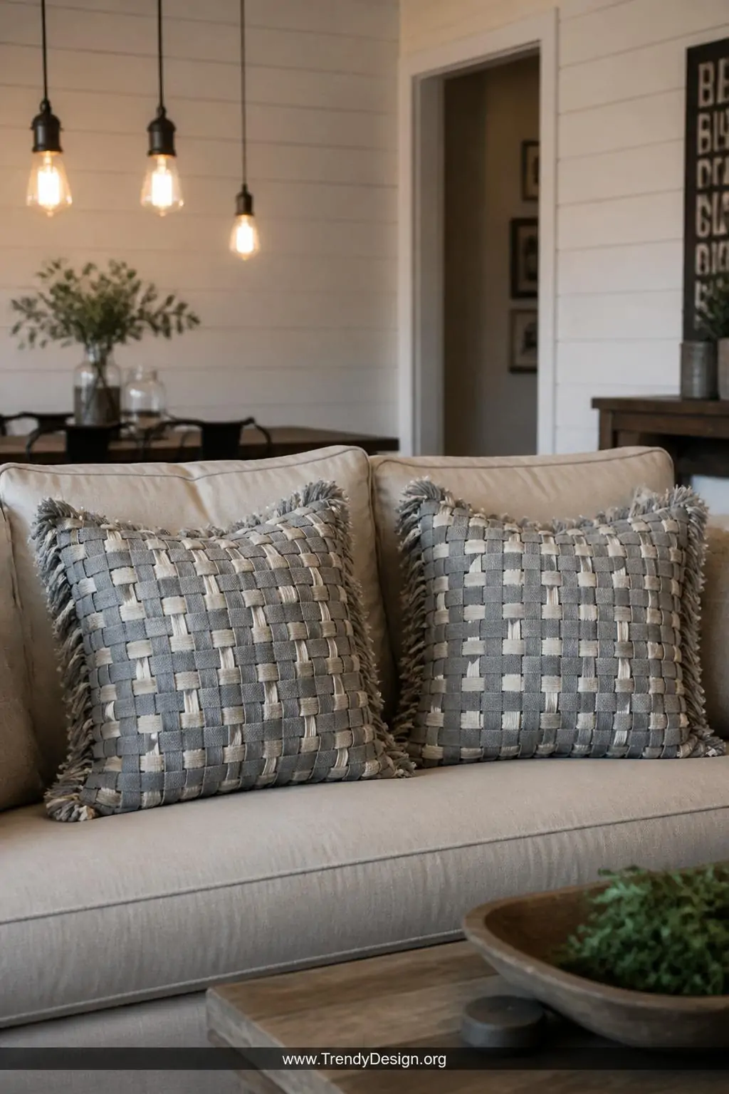 A styled linen sofa in a soft neutral living room lit by warm Edison bulb pendant lighting, featuring two oversized woven pil