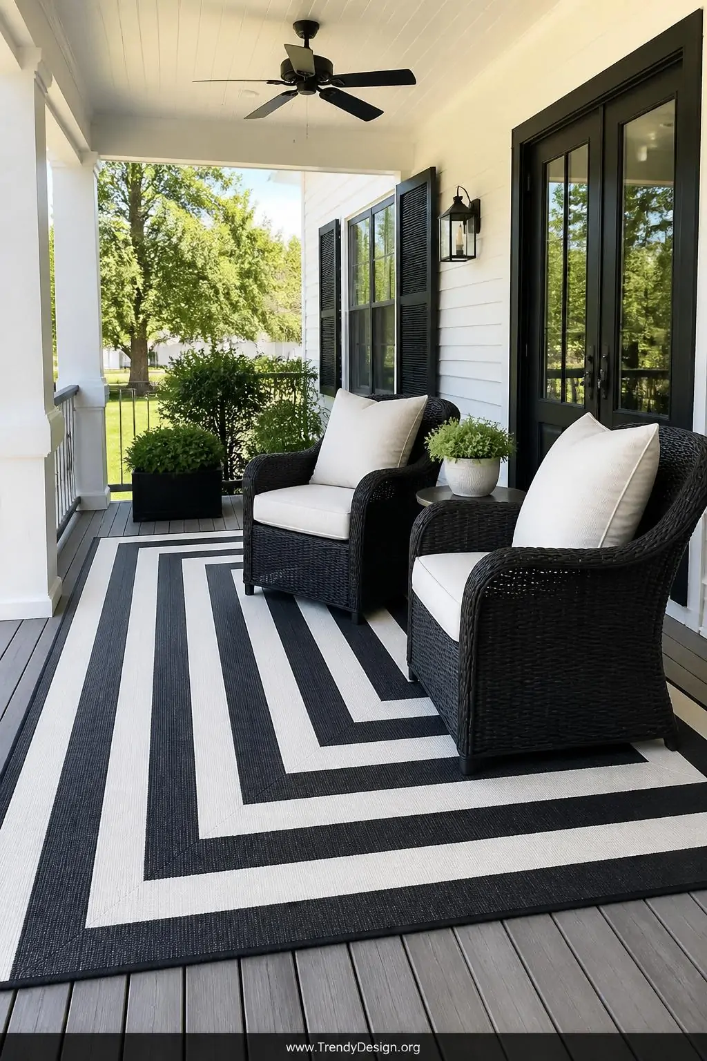 Wide shot of a polished front porch seating area anchored by a large oversized black-and-white striped outdoor rug beneath tw