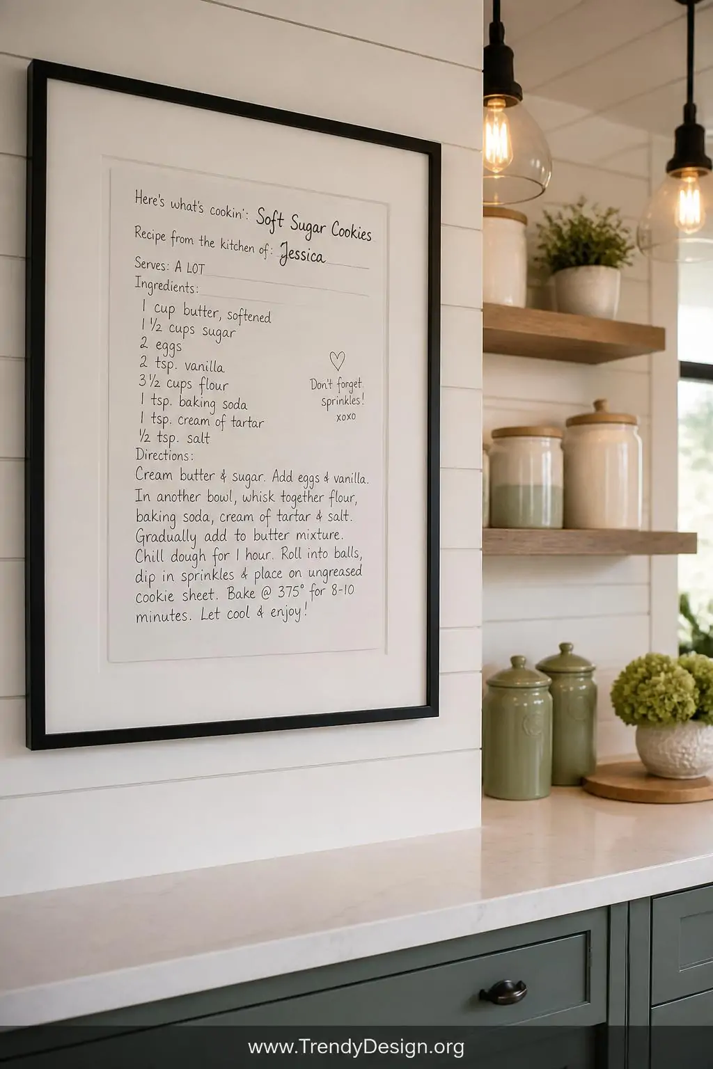 A medium shot of a bright kitchen wall featuring a beautifully framed black-and-white print of a child's handwritten recipe c