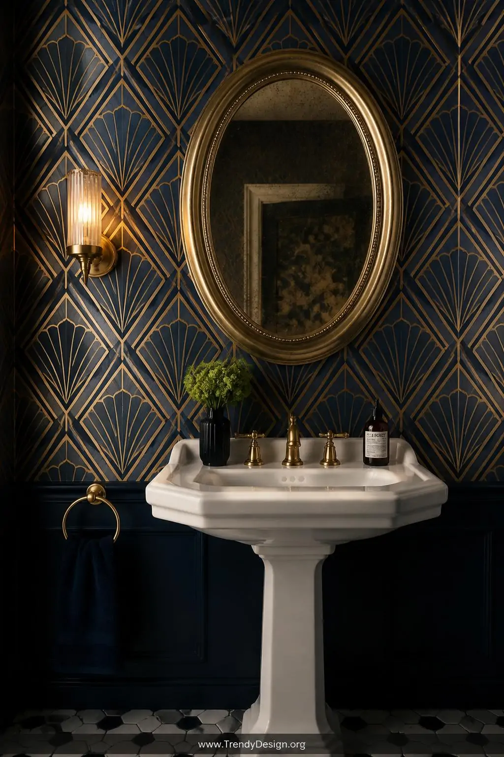 Crisp Art Deco gold and navy geometric wallpaper with repeating fan shapes and gilded diamond lines framing a vintage pedestal sink and oval antiqued mirror in a glamorous bathroom, a single brass sconce casting warm directional light across the metallic pattern, medium architectural shot, photorealistic.