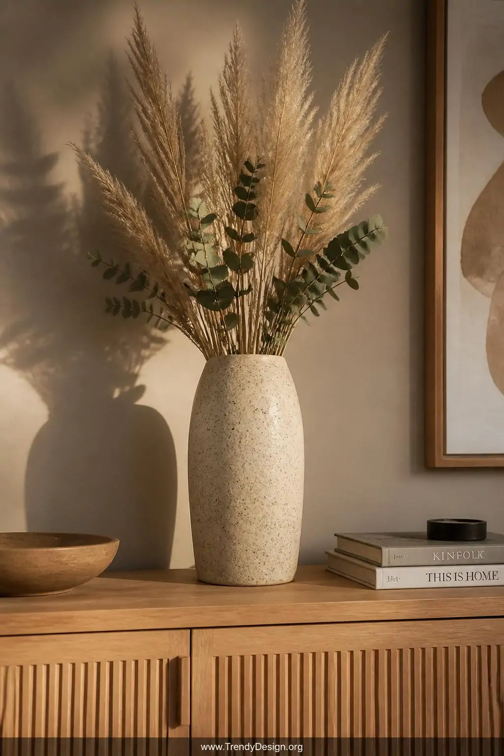 Tall speckled clay pinch pot vase with black fleck detailing holding dried pampas grass and eucalyptus on a natural oak sideboard against a warm greige wall, golden afternoon light, medium shot