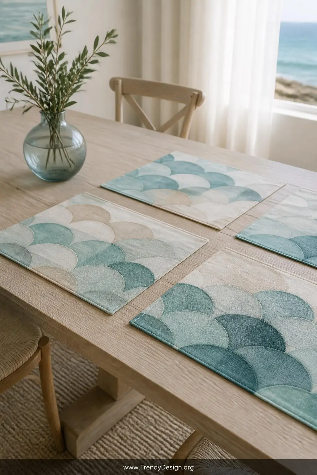 Canvas placemats stamped with overlapping teal and sandy beige wave scallop patterns set on a bleached oak dining table, coastal coastal light through sheer curtains, a full set of four placemats showing varied color intensity, wide shot capturing the layered watercolor-like sophistication