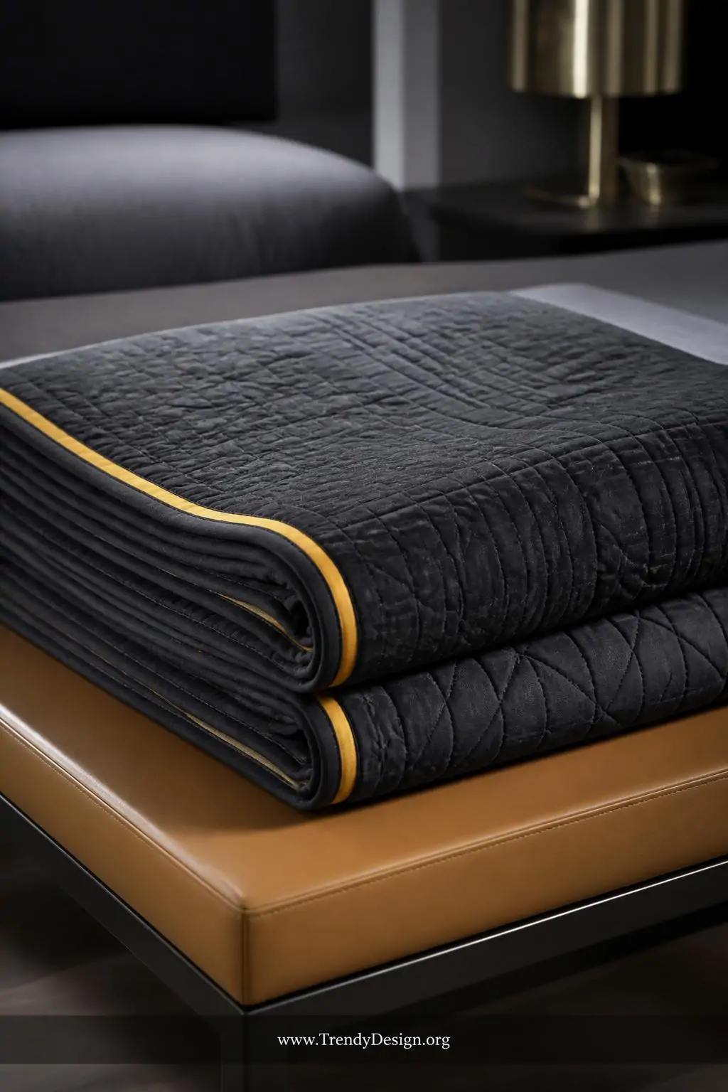 Decorative flange binding with a crisp mustard yellow contrasting strip peeking out between a deep charcoal quilt top and a coordinating solid binding on a neatly folded show quilt displayed on a sleek modern bedroom bench, cool directional spotlight, closeup shot revealing the precise quarter-inch line of color that frames the entire quilt like an elegant picture mat.
