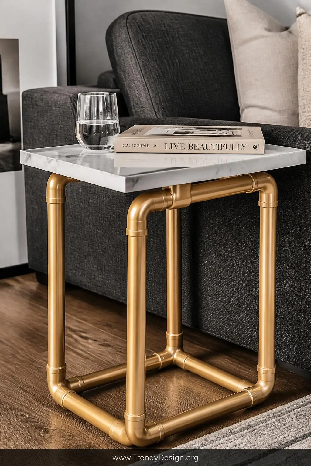 Gold-painted PVC pipe side table with a marble-contact-paper-wrapped wooden top beside a charcoal linen sofa, styled with a glass of water and a hardcover book, soft diffused afternoon light, closeup shot highlighting the glamorous pipe leg detail.