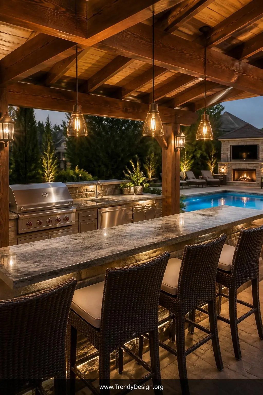 Freestanding pergola sheltering a built-in outdoor kitchen and granite bar counter beside a sparkling pool, stainless steel grill and mini fridge tucked beneath cedar beams, Edison bulb pendant lights overhead, wicker bar stools lined up at the counter, warm evening light glowing across polished stone surfaces, medium shot from the bar seating perspective.