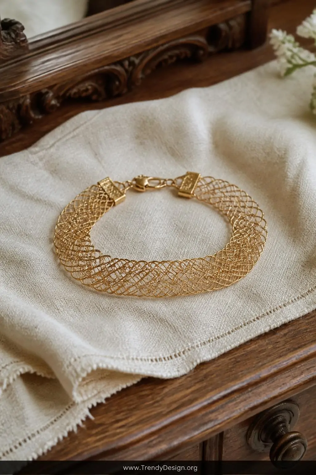Filigree wire weave bracelet laid flat on aged ivory linen fabric on an antique wooden dressing table, soft diffused natural light, intricate over-under lacy openwork pattern in fine gold-filled wire resembling delicate heirloom lacework, closeup
