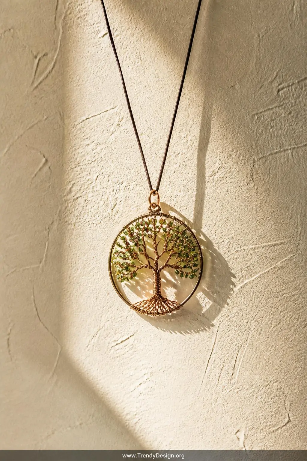 Copper wire Tree of Life pendant with tiny green seed bead leaves hanging from a thin leather cord against a textured white plaster wall, warm golden side light casting delicate wire shadows, medium wide shot