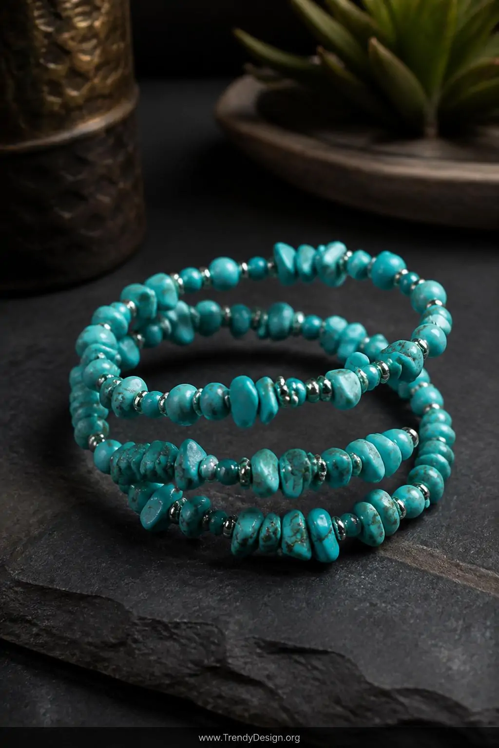 Turquoise chip bead memory wire cuff with metallic seed bead accents coiled loosely on a dark slate stone display surface, moody side lighting, medium shot emphasizing the organic mixed textures of smooth rounds and irregular chip beads spiraling across the wire.