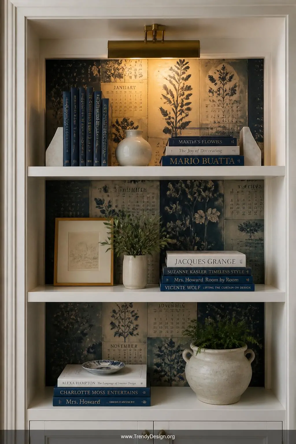 Inside a tall white painted bookcase a dramatic accent panel of layered calendar pages in deep indigo botanical illustrations