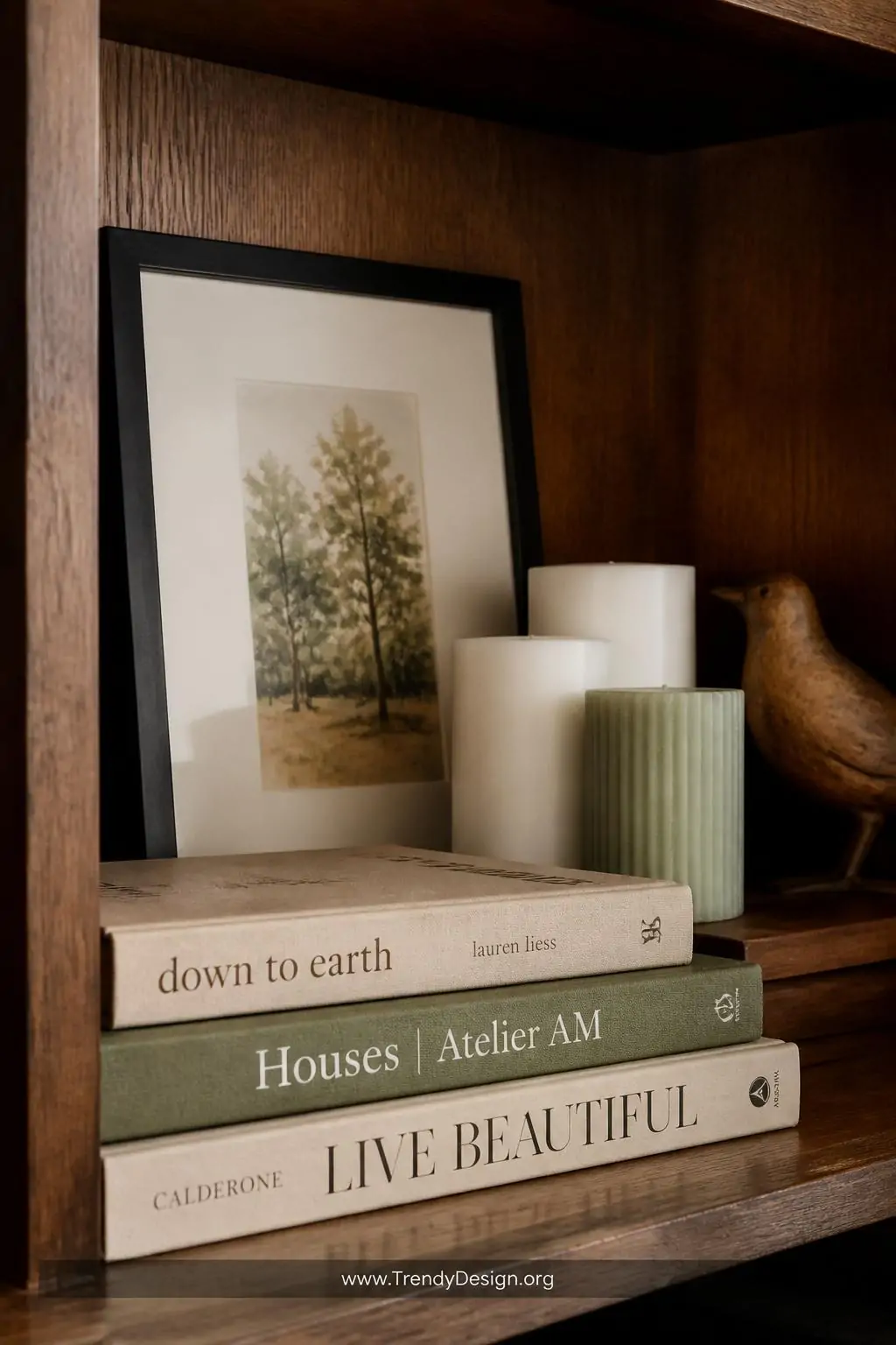 Close-up shot of a deep oak bookshelf section demonstrating intentional layering — a small watercolor print in a thin black f