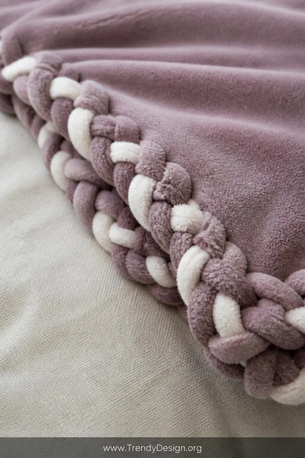 A closeup photorealistic detail shot of a finished braided-edge no-sew fleece blanket in dusty mauve and ivory, the intricate