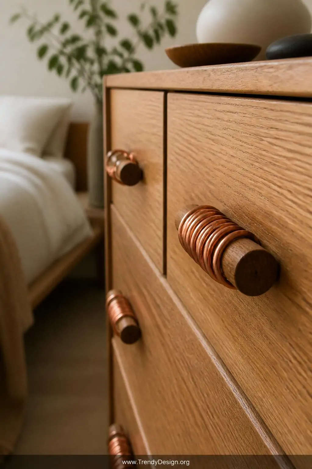 Thin copper wire bangles coiled around natural wood drawer pulls on a honey-toned oak dresser in a Scandinavian bedroom, handcrafted designer detail, soft diffused morning light warming the copper tones against the grain, closeup.