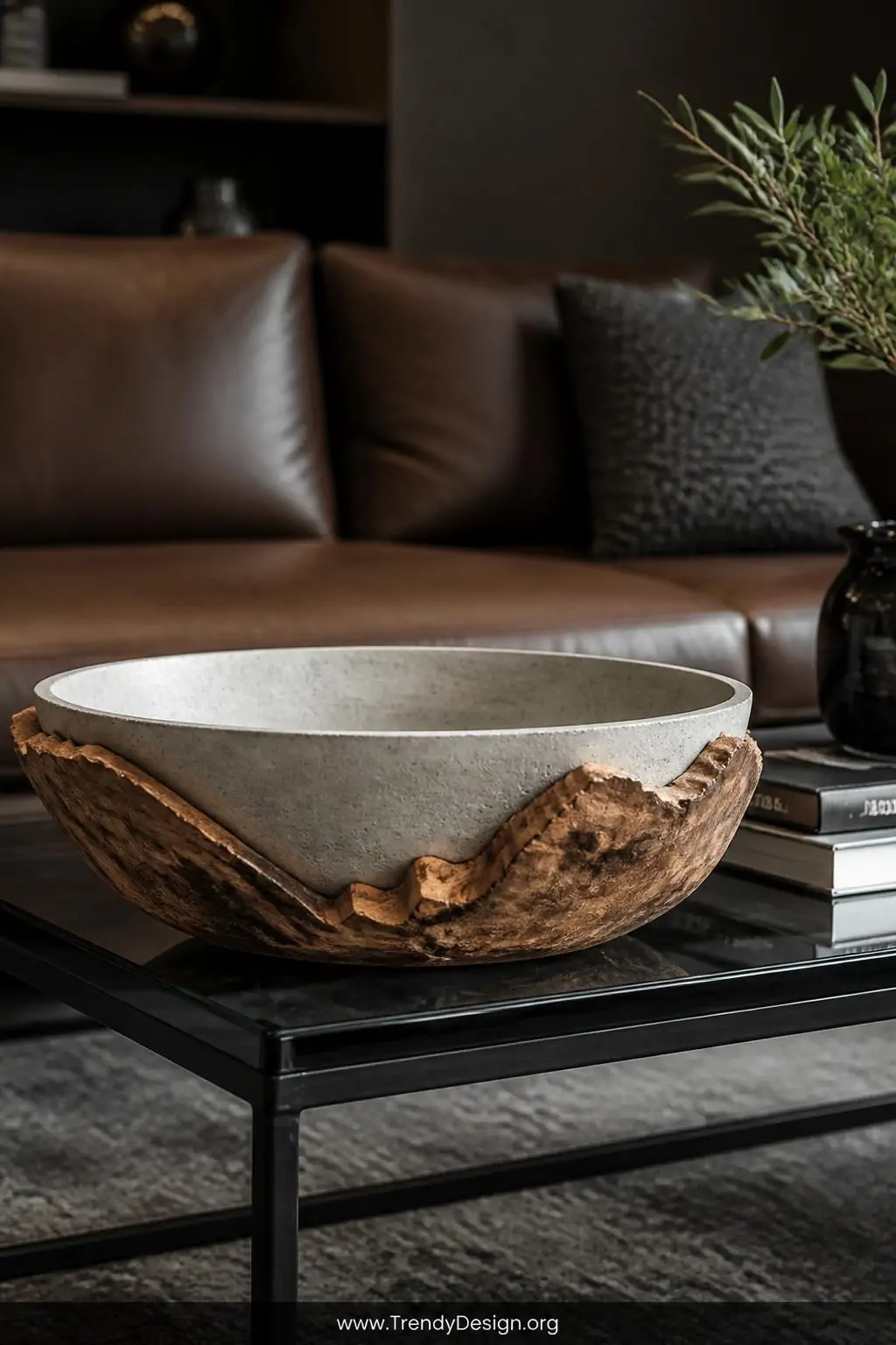A striking concrete bowl with a live-edge dark walnut wooden base sits dramatically on a black steel and glass coffee table, 