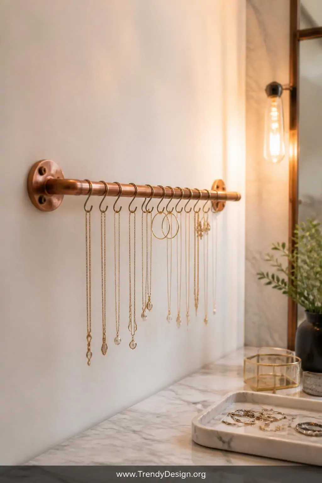 Horizontal copper pipe jewelry organizer mounted between two copper wall flanges in a marble-tiled boutique bedroom, delicate gold necklaces and earrings hanging against a soft white wall, warm vanity lighting, closeup.
