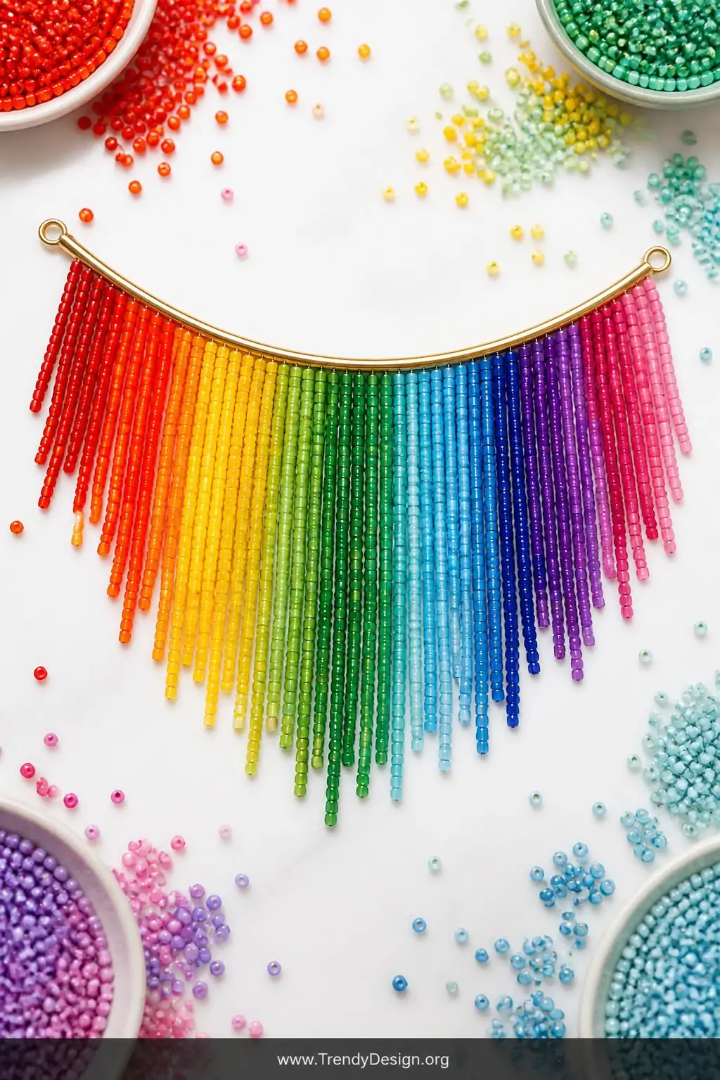 Rows of rainbow Miyuki bead fringe strands in full spectrum graduated color arranged on a curved gold finding, displayed flat on a bright white surface with scattered colorful seed beads surrounding them, bright cheerful overhead light, wide flat-lay shot.