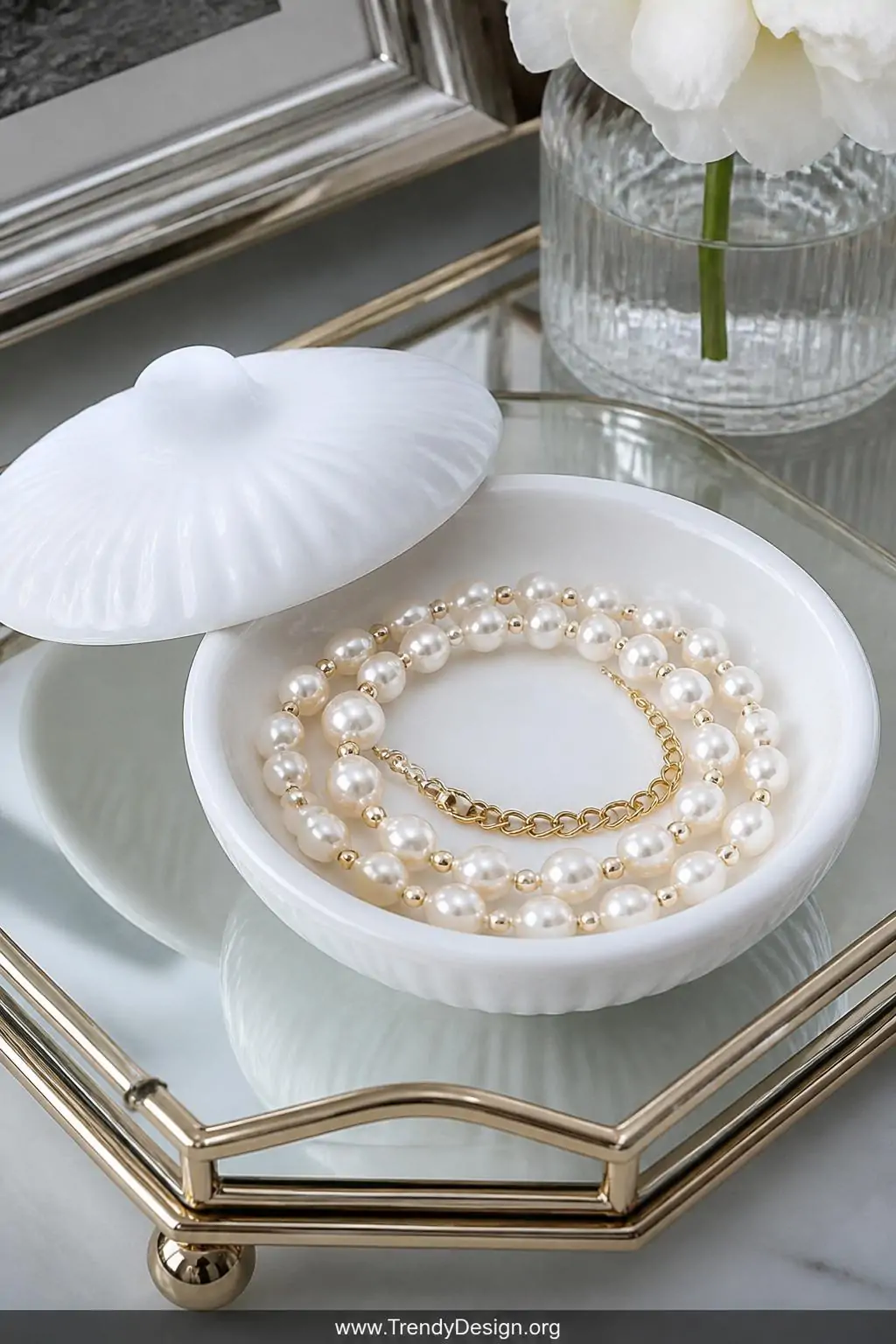 Faux pearl and gold spacer bead choker coiled elegantly inside an open white ceramic ring dish on a glass vanity tray, cool diffused natural light, closeup revealing lustrous pearl surfaces and delicate crimp bead finish