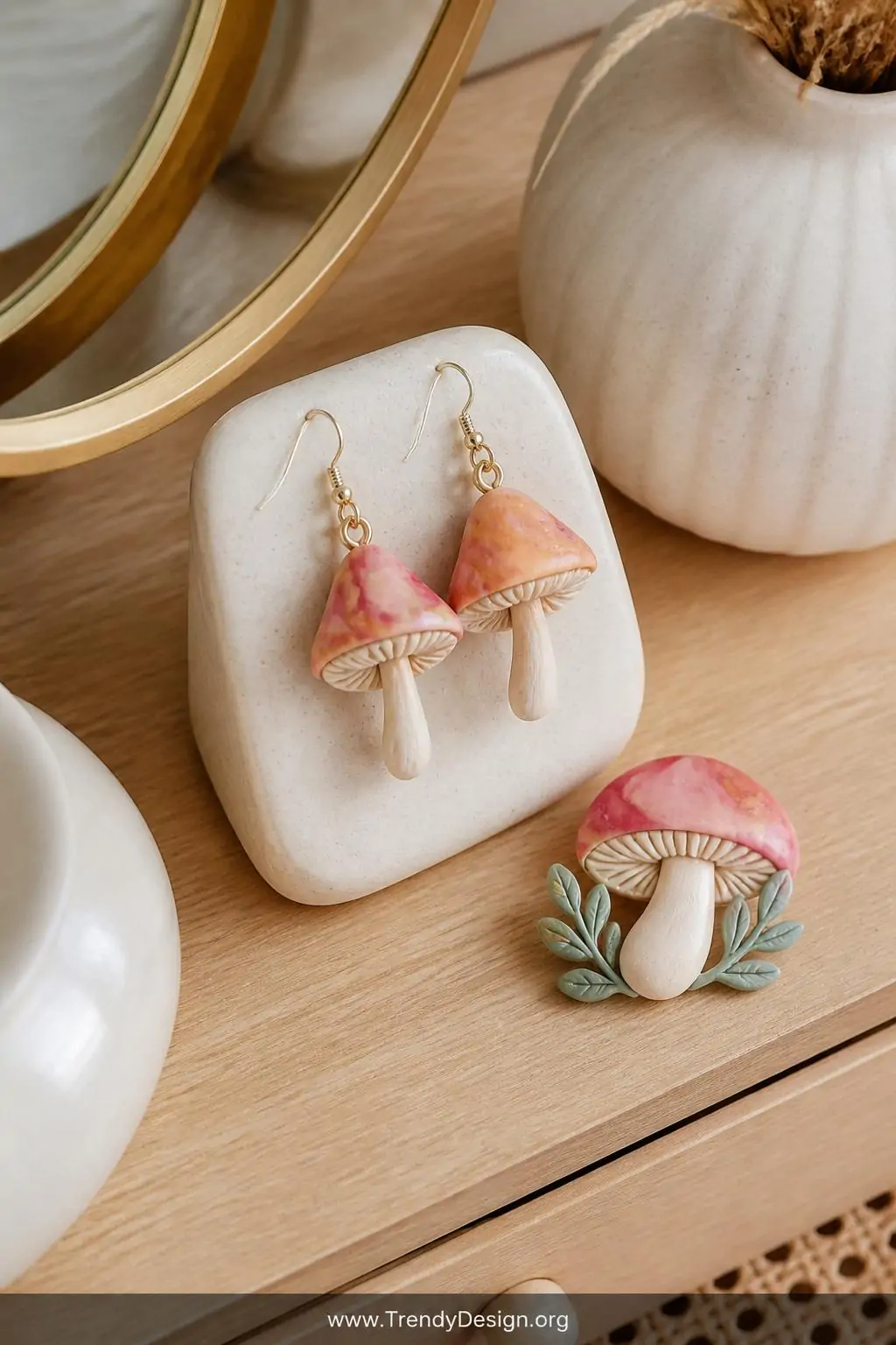Pair of delicate polymer clay mushroom earrings with marbled gradient caps in terracotta and dusty rose displayed on a small ceramic jewelry stand on a light oak vanity beside a matching clay mushroom brooch, soft diffused studio-style light, extreme closeup styled flat lay, photorealistic interior design